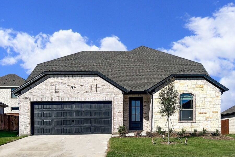 Single-story suburban home with a stone facade and dark shingled roof under a cloudy sky.