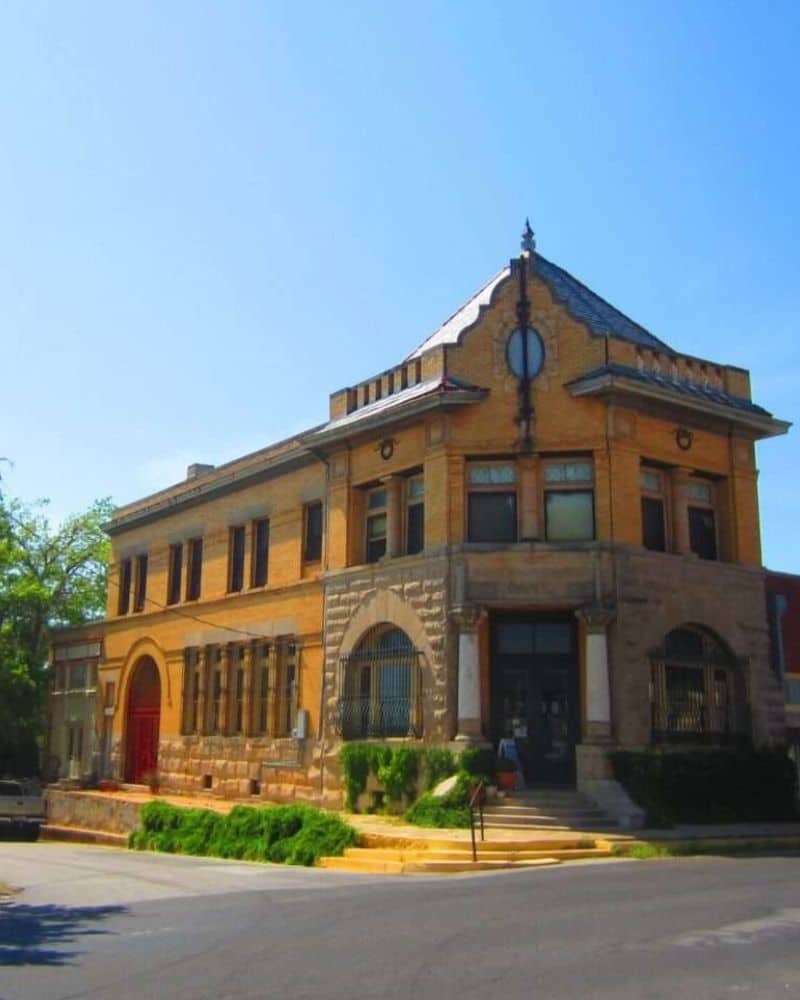 Historic two-story brick building with a stone foundation, large windows, and a decorative gable under a clear blue sky.