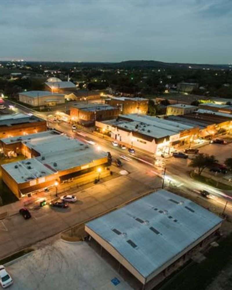 Aerial view of a small town at dusk with streetlights and buildings illuminated.